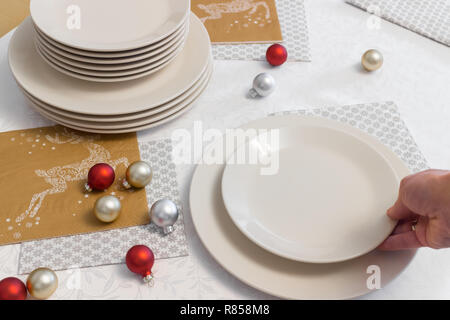 Hand is putting plate on holiday table. Preparing Christmas table Stock Photo