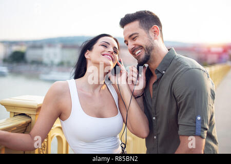Happy young urban couple sharing music by headphones at outdoors Stock Photo