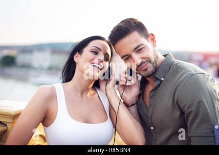 Urban couple sharing headphones and listening music at outdoors in sunset Stock Photo