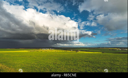 Heavy rainy clouds over the Northern Ireland field. Stunning countryside landscape. Green grass covered meadow under the colorful sky before the rain. Panoramic view of the wild virgin nature. Stock Photo