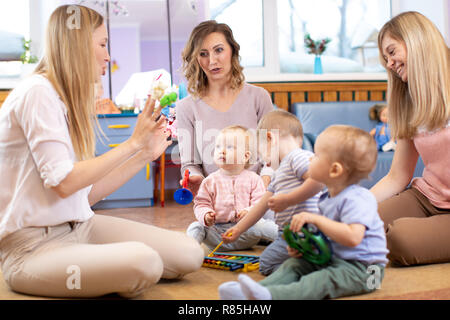 Mentor and 1 years old babies playing with educational toys in kindergarten or daycare centre Stock Photo