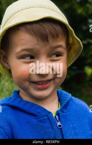 A little boy in a bright hat and blue sweater mow down his eyes and smiles Stock Photo
