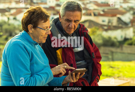 Mature woman with glasses and winter clothes shows something on her smartphone to her husband Stock Photo
