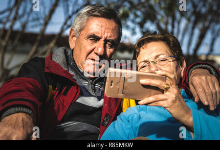 Mature woman with smartphone embraced by her husband while both sitting in park and watching online video Stock Photo