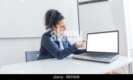 Portrait of a normal business woman pointing at the white laptop screen in a office desk. With copy space. Dressing professionally looking at the computer Stock Photo