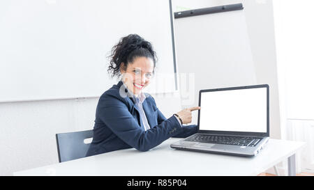 Portrait of a normal business woman pointing at the white laptop screen in a office desk. With copy space. Dressing professionally smiling & looking at the camera Stock Photo