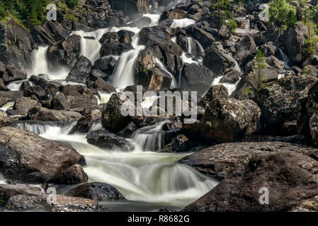Beautiful waterfall with smooth water falling among the rocks and black stones in the mountains, shot on long exposure Stock Photo