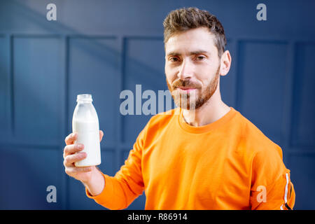 Conceptual portrait of a sports man in bright sweater drinking milk from the bottle on the blue background Stock Photo