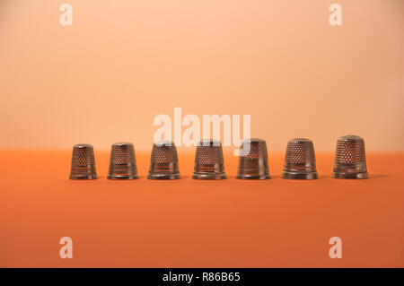 Aligned group of thimbles of different sizes on an orange surface with a blurred background Stock Photo