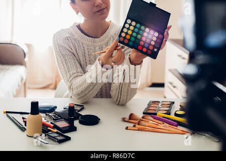Young woman professional beauty vlogger or blogger recording make up tutorial using camera and tripod at home Stock Photo