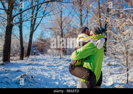 Happy couple in love walking and hugging in winter forest. Man holding girlfriend and kissing. Young people having fun Stock Photo