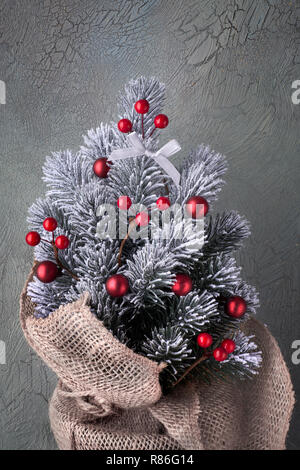 Small Christmas tree in sackcloth decorated with red baubles and berries on neutral textured background Stock Photo