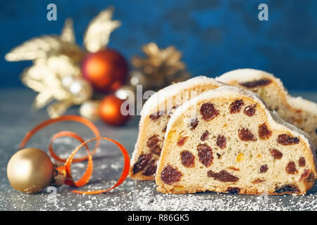 Christmas stollen on white-blue festive background with golden decorations. Traditional German dessert for Christmas celebration. Stock Photo