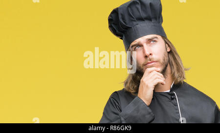 Young handsome cook man with long hair over isolated background with hand on chin thinking about question, pensive expression. Smiling with thoughtful Stock Photo