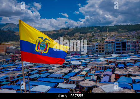 OTAVALO, ECUADOR, NOVEMBER 06, 2018: Beautiful Ecuadorian flags waving in a gorgeous sunny day with huts located in the street market in Otavalo with a mountain behind in Otavalo Stock Photo