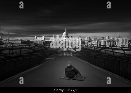 Homeless person sitting on millennium bridge looking towards St Pauls in the city of London Stock Photo