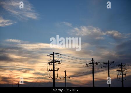 Substation electrical supply distribution, utility poles and high voltage power supply wires silhouette at sunset in Wyoming, USA Stock Photo