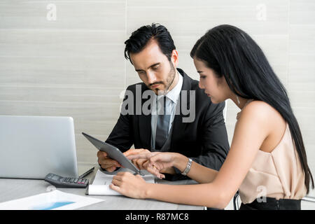 Couple of young business people working at modern office, two coworkers discussing fun project over tablet, little team of businesspeople smiling and  Stock Photo