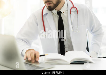 Doctor using laptop and electronic medical record (EMR) system. Digital database of patient's health care and personal information on computer screen. Stock Photo