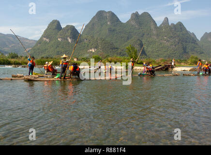 Tourists floating on punted bamboo rafts on Yulong River, Yangshuo, China. Punter using long pole to steer raft, green hills along river. Copy space. Stock Photo