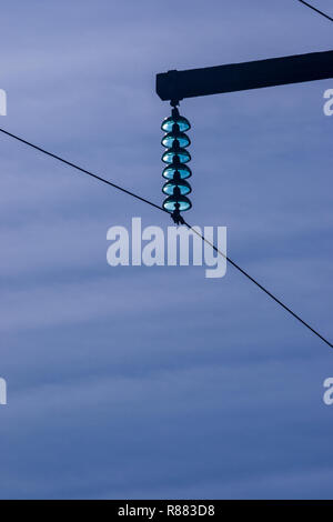 115 Kv High tension power lines supported high above the ground using wooden poles on a clear sunny day with a commercial jet passing above. Stock Photo