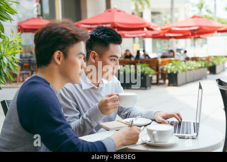 Two young businessmen are chatting in a coffee shop. - Image Stock Photo