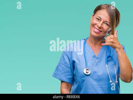 Middle age senior nurse doctor woman over isolated background smiling doing phone gesture with hand and fingers like talking on the telephone. Communi Stock Photo
