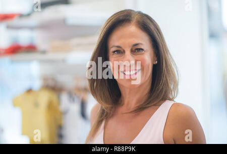 Beautiful middle age hispanic woman standing with smile on face at clothes store. Shop owner and shop assistant smiling confident and cheerful Stock Photo