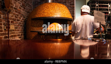 A chef is putting a handmade fresh pizza in a wood burning brick oven pizza. Stock Photo