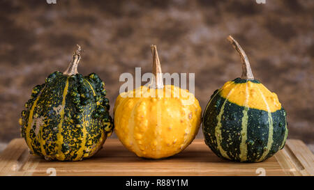 Three pumpkins on a table with wooden cutting board and a rustic background. Stock Photo