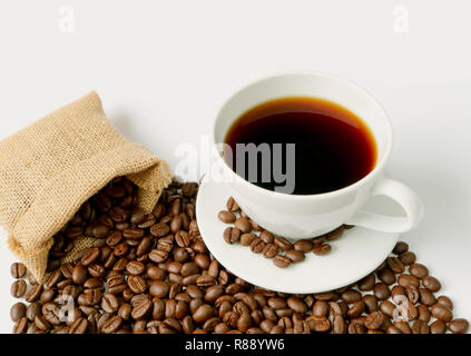 Cup of hot black coffee with heap of roasted coffee beans scattered from burlap sack on white background Stock Photo