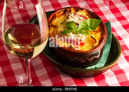 Woodfire baked traditional rustic italian  style lasagna in a clay pot with white wine served on table Stock Photo