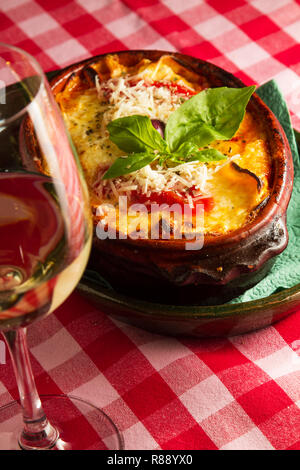 Woodfire baked traditional rustic italian  style lasagna in a clay pot with white wine served on table Stock Photo