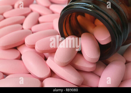 Heap of light pink color oval shaped pills scattered from glass bottle Stock Photo