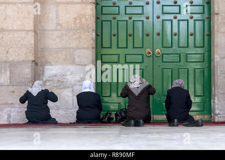 four women pray on their knees in front of the green closed door of the old mosque Dome of the Rock in the Muslim quarter of the old city of Jerusalem Stock Photo