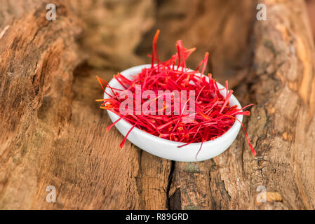 White ceramic bowl of red saffron threads isolated on wooden background and viewed in close-up and high angle Stock Photo