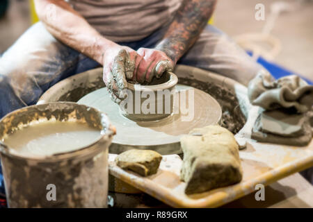 Man making pot of clay in pottery, forming the shape of clay, during pottery production process. Viewed in close-up with clay pieces and bucket of wat Stock Photo