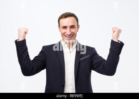 Pleased and happy young italian man is smiling broadly and showing victory sign with both hands. Stock Photo