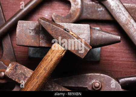 Old rusty rugged anvil, hammer other blacksmith tools on brown natural wooden background. Flat lay top view. Stock Photo