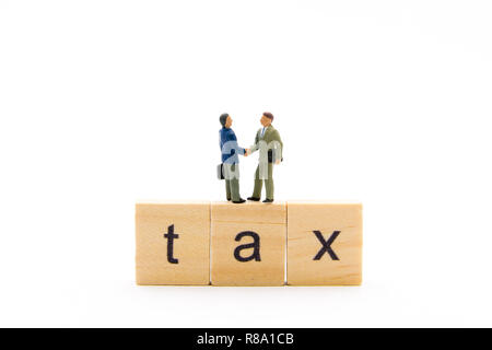 Miniature figures as business men standing over wooden blocks with letters making Tax word and shaking hands, isolated on white background Stock Photo