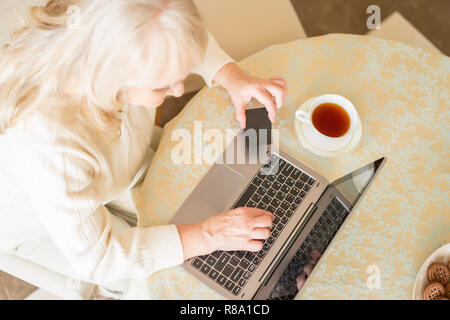 Top Vies On Elderly Woman Making Paying Transactions With The Help Of A Credit Card Over A Cup Of Tea. Stock Photo