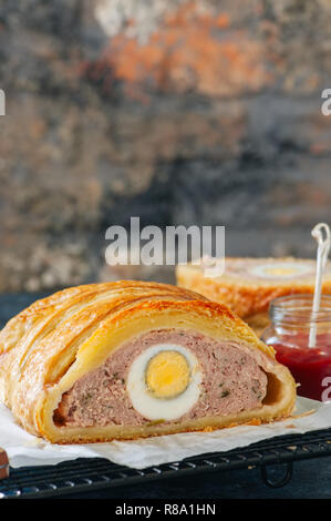 Turkey meatloaf with egg filling in a puff pastry served on a wire rack. Blue stone backdrop. Stock Photo