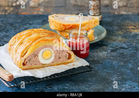 Turkey meatloaf with egg filling in a puff pastry served on a wire rack. Blue stone backdrop. Stock Photo