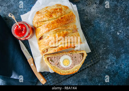 Turkey meatloaf with egg filling in a puff pastry served on a wire rack. Blue stone backdrop. Stock Photo