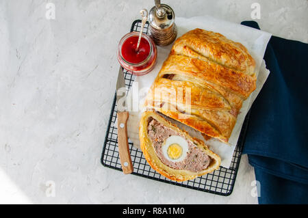 Turkey meatloaf with egg filling in a puff pastry served on a wire rack. Blue stone backdrop. Stock Photo