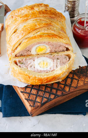Turkey meatloaf with egg filling in a puff pastry served on a wire rack. Blue stone backdrop. Stock Photo