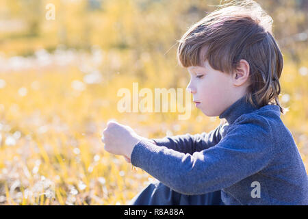 A child sits and thinks. Boy dreaming on grass and sad. Stock Photo