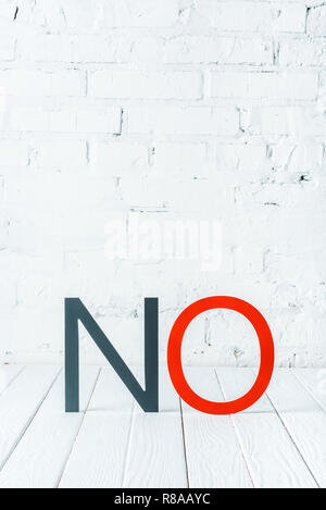 "no" lettering with decorative black and red letters on white wooden surface with brick wall at background Stock Photo