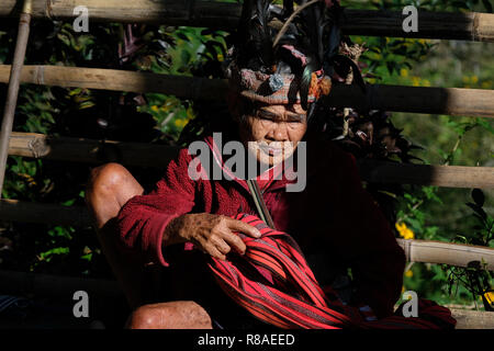 An elderly Ifugao man wearing headdress adorned with feathers at the Banaue Rice Terraces in northern Luzon, Philippines. In the past the Ifugao also known as the Ifugaw, Ipugao, Yfugao were feared head-hunters, just as other tribes in the mountainous regions of northern Luzon. Stock Photo