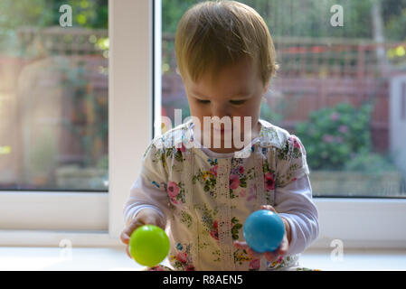 Few Months Old Baby Sitting And Holding Blue And Green Ball Glass
